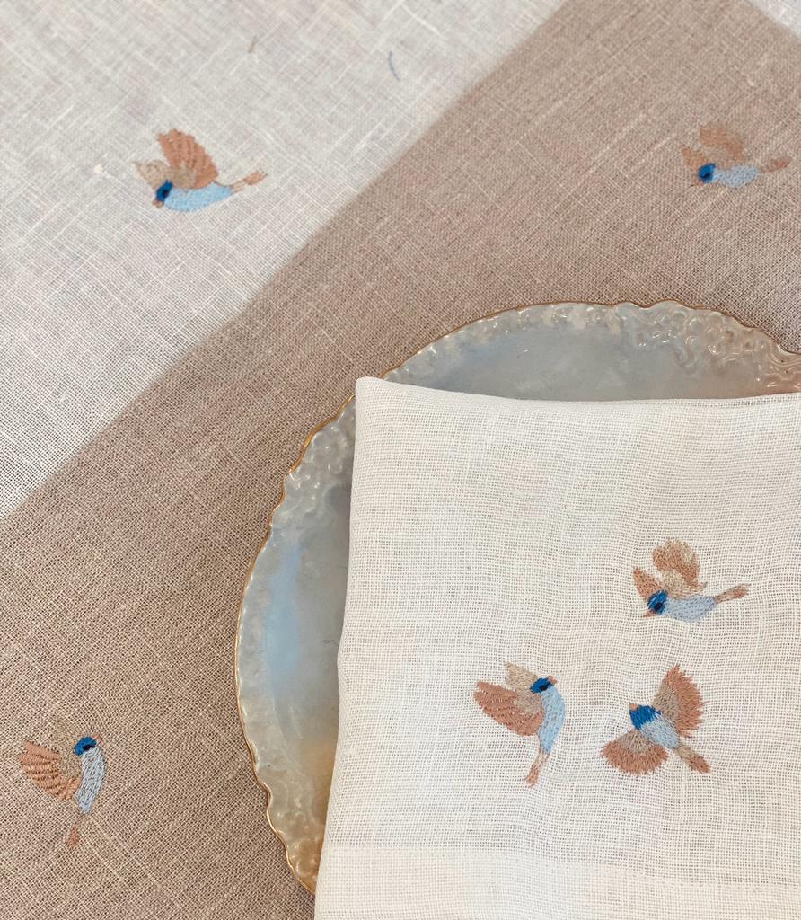 Napkin with embroidered bird design on linen placemat with bird emroidery.