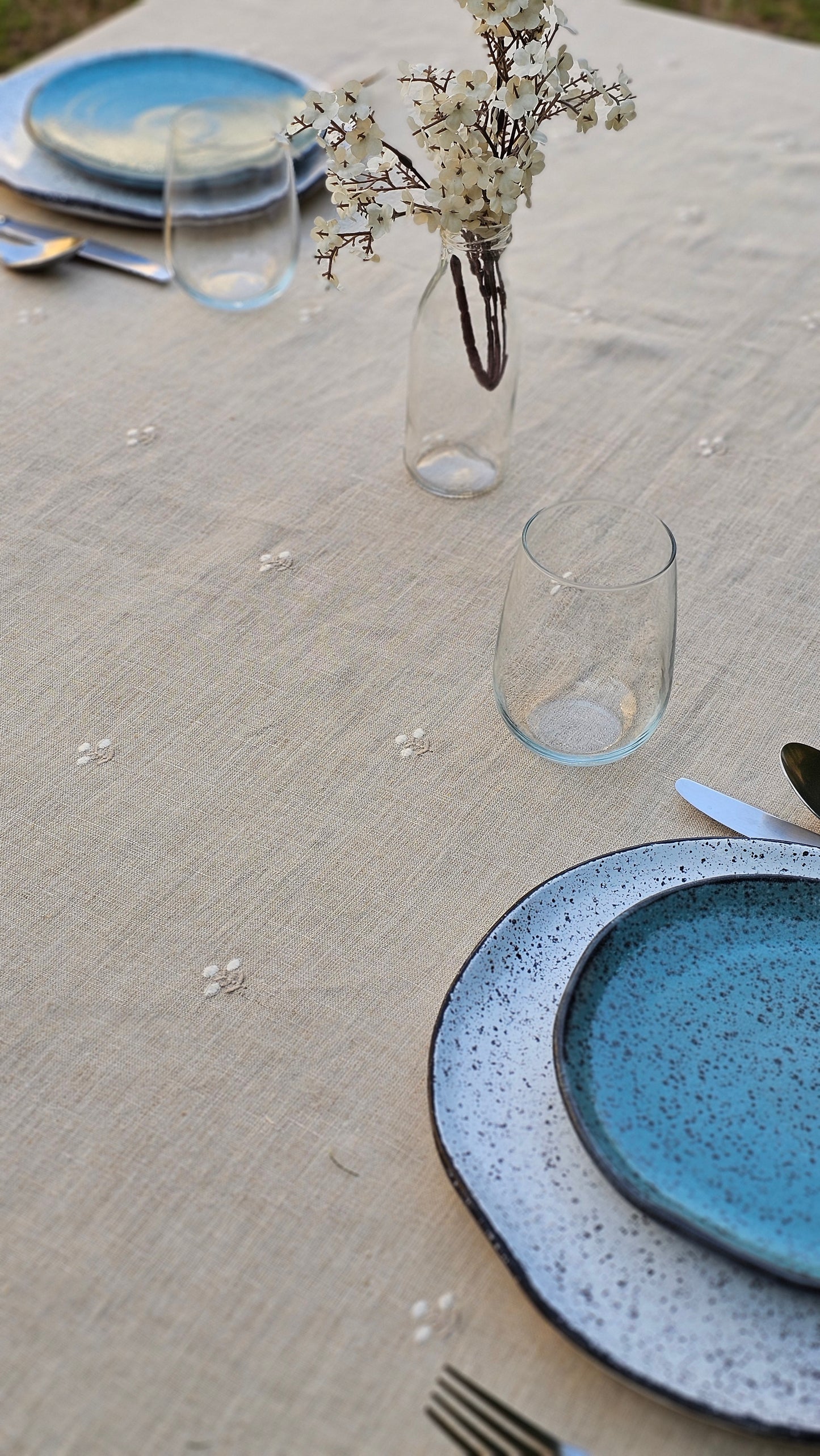 Table setting with blue ceramic plates and glasses on an Egyptian linen tablecloth with minimal floral embroidery.