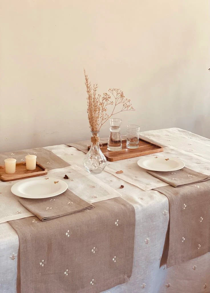 Dining table setting with beige Egyptian linen tablecloth with embroidery, plates, and decorative elements.