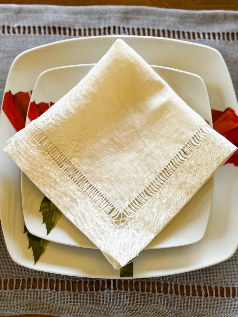 Handmade Egyptian linen off-white napkin on a stack of white plates with a decorative edge
