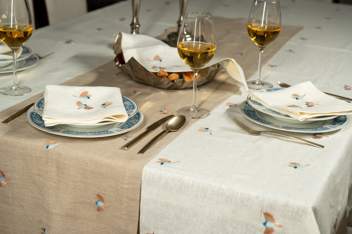 Dining table set with plates, glasses, and cutlery on a patterned Egyptian linen tablecloth with birds embroidery.