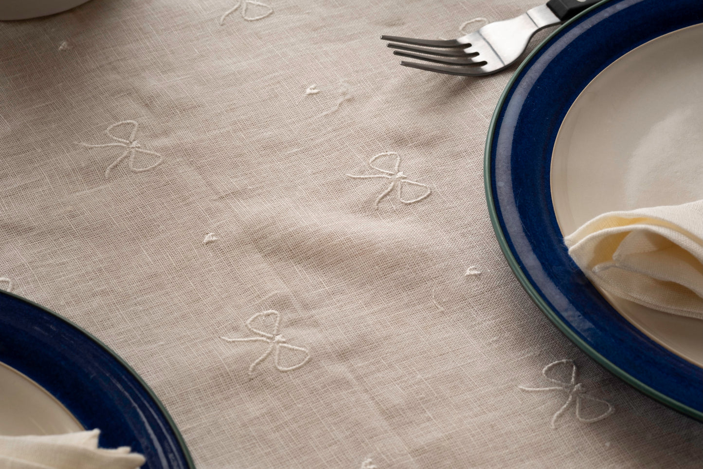 Off white tablecloth with embroidered ribbon embroidery and blue plates on a table.