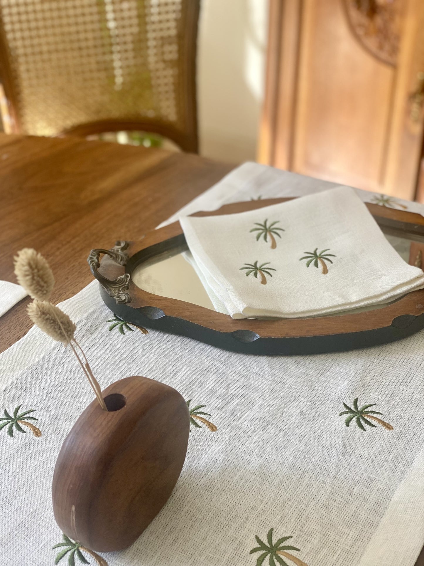 Wooden holder with dried plants on a table with Egyptian linen palm tree patterned napkins and runner.