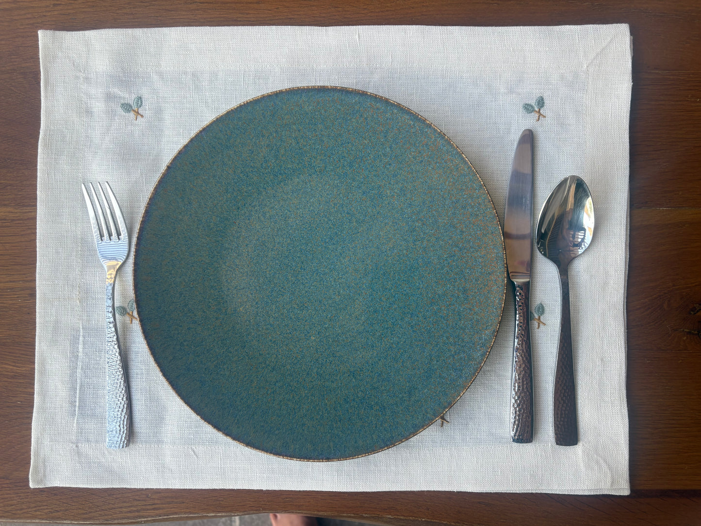 Teal plate with silverware on a white placemat on a wooden table