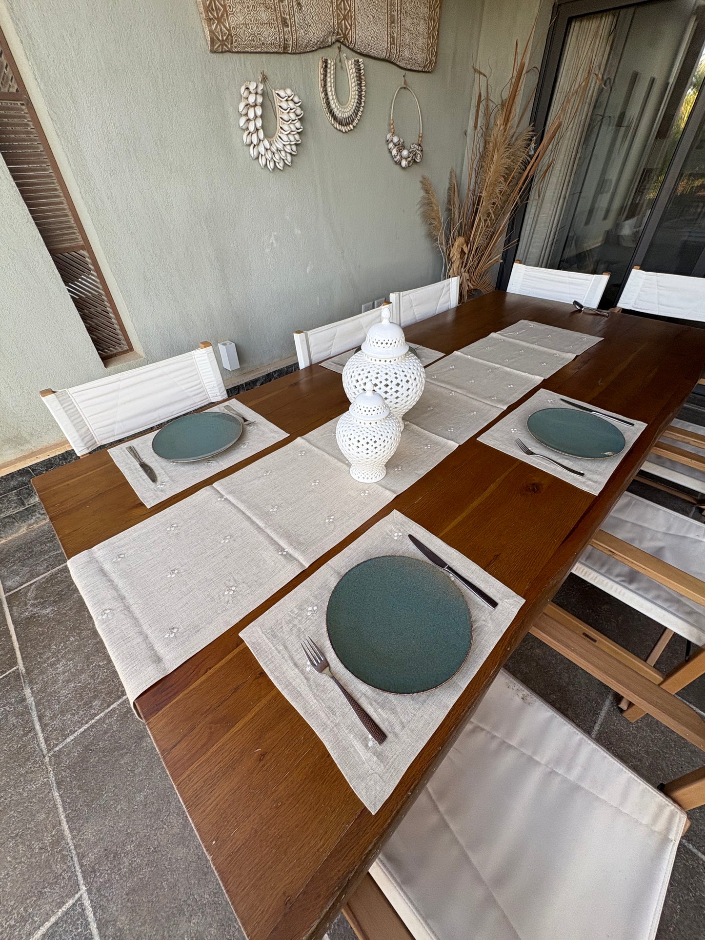 Dining table set with linen placemats, plates, cutlery, and a vase on a stone patio.