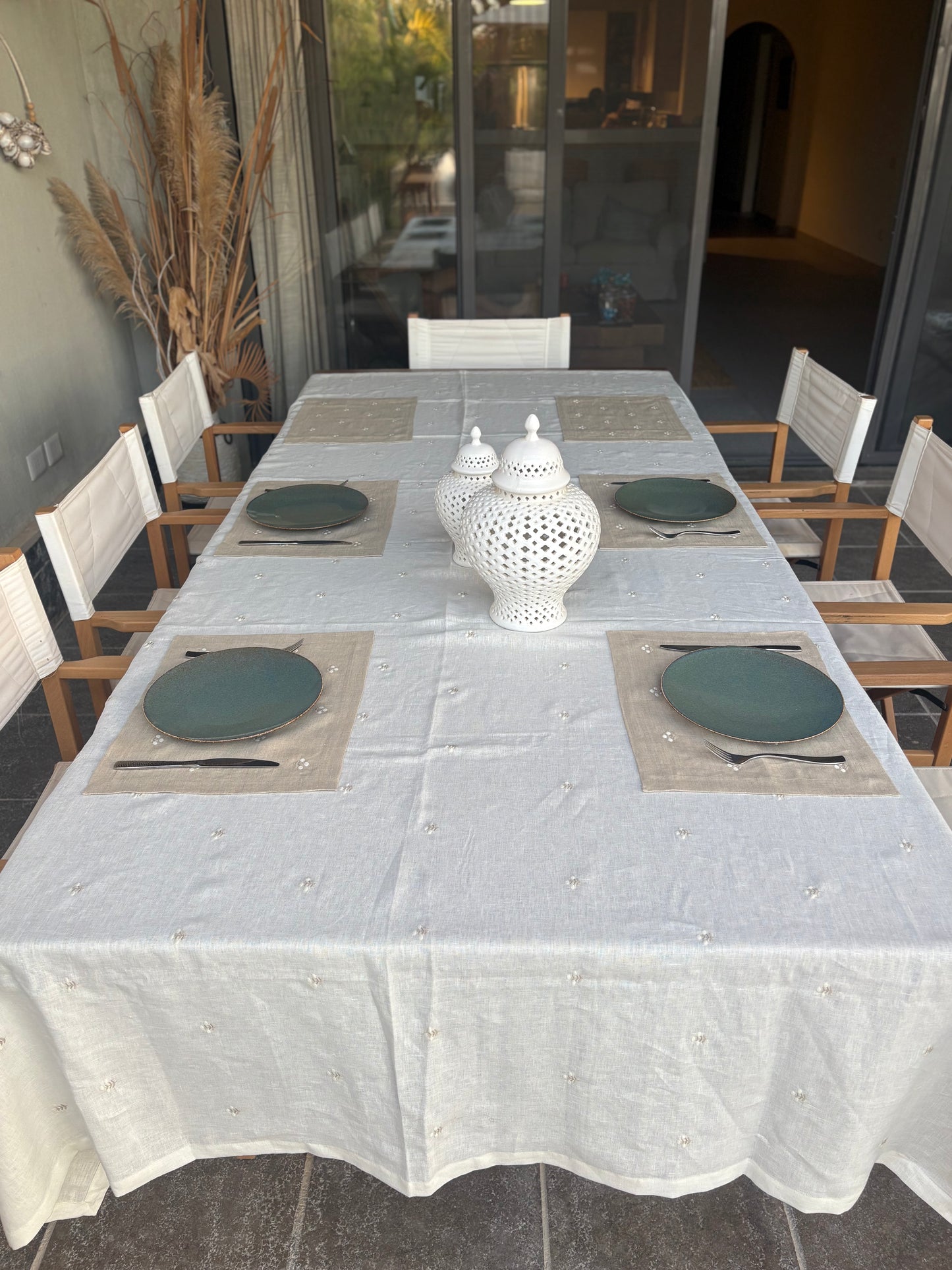 Dining table set with Egyptian linen placemats and decorative vases in a room with large windows.