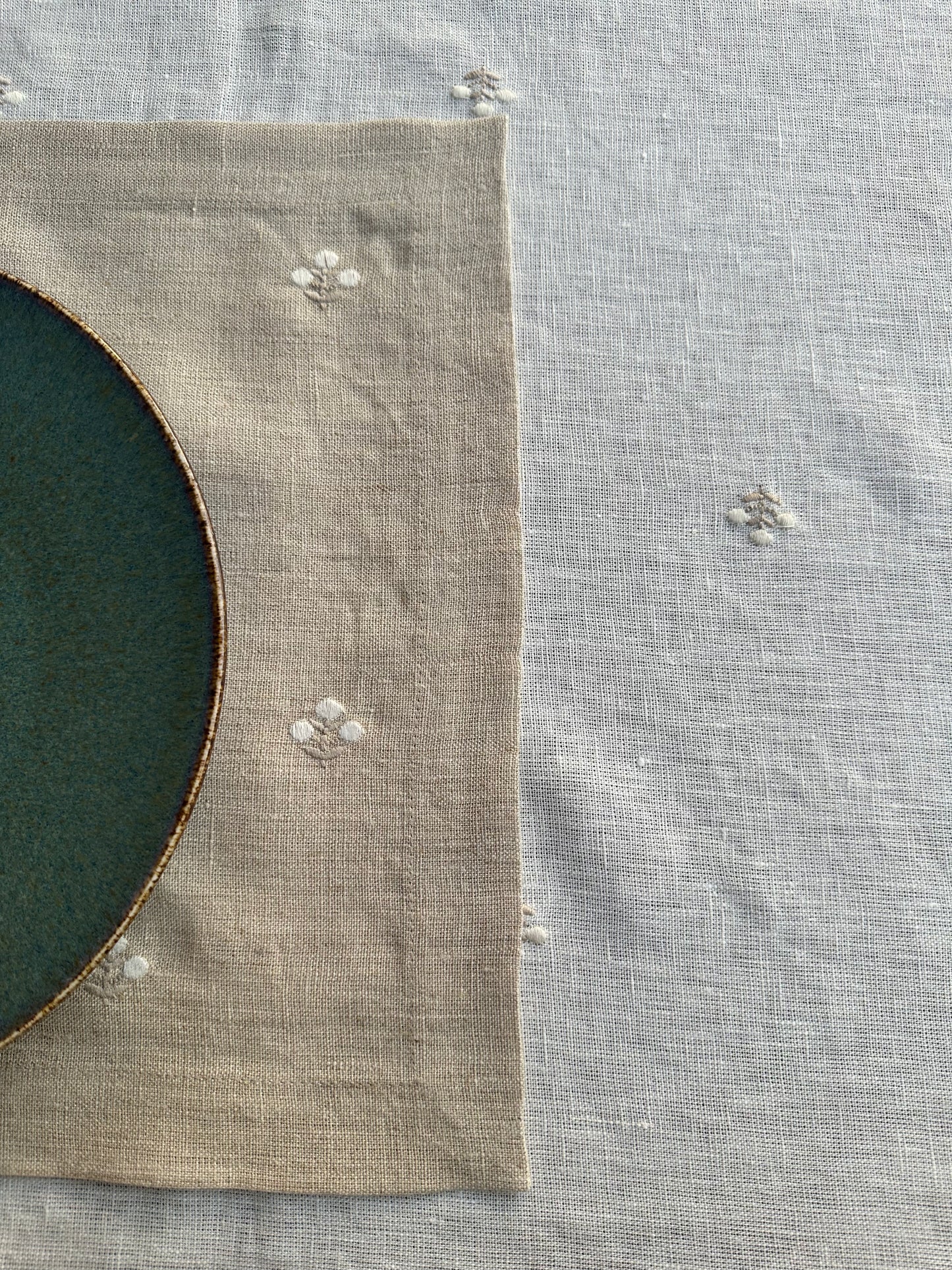 Close-up of a green plate with a brown rim on a beige linen placemat with minimal floral embroidery.