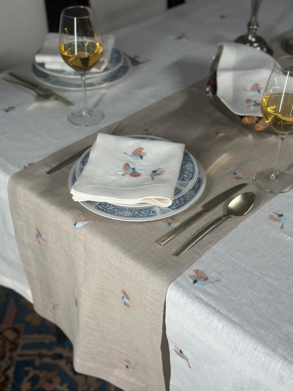 Dining table setting with plates, glasses, and cutlery on a Egyptian linen tablecloth with birds embroidery.