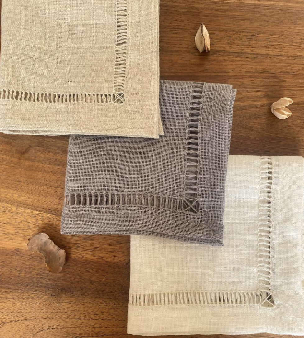Three handmade Egyptian linen napkins with hemstitched edges on a wooden surface.