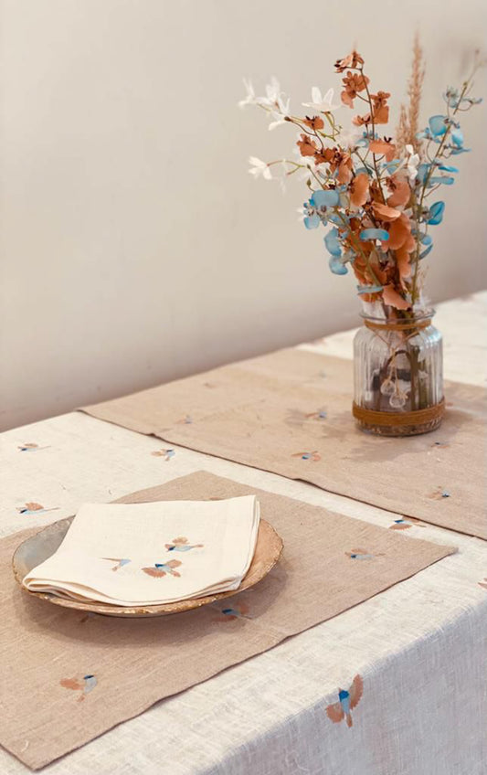 Table setting with a vase of flowers, plates, placemats, and napkins on a neutral background