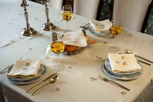 Dining table set with plates, glasses, and cutlery on an Egyptian linen tablecloth with bird embroidery.