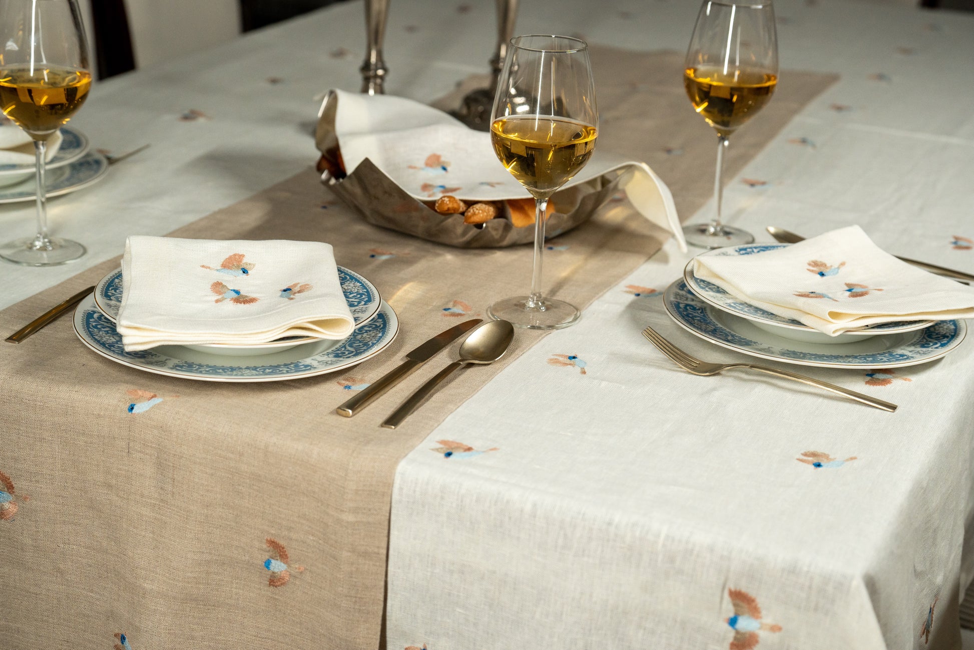 Dining table set with plates, glasses, and cutlery on a patterned Egyptian linen tablecloth with birds embroidery.