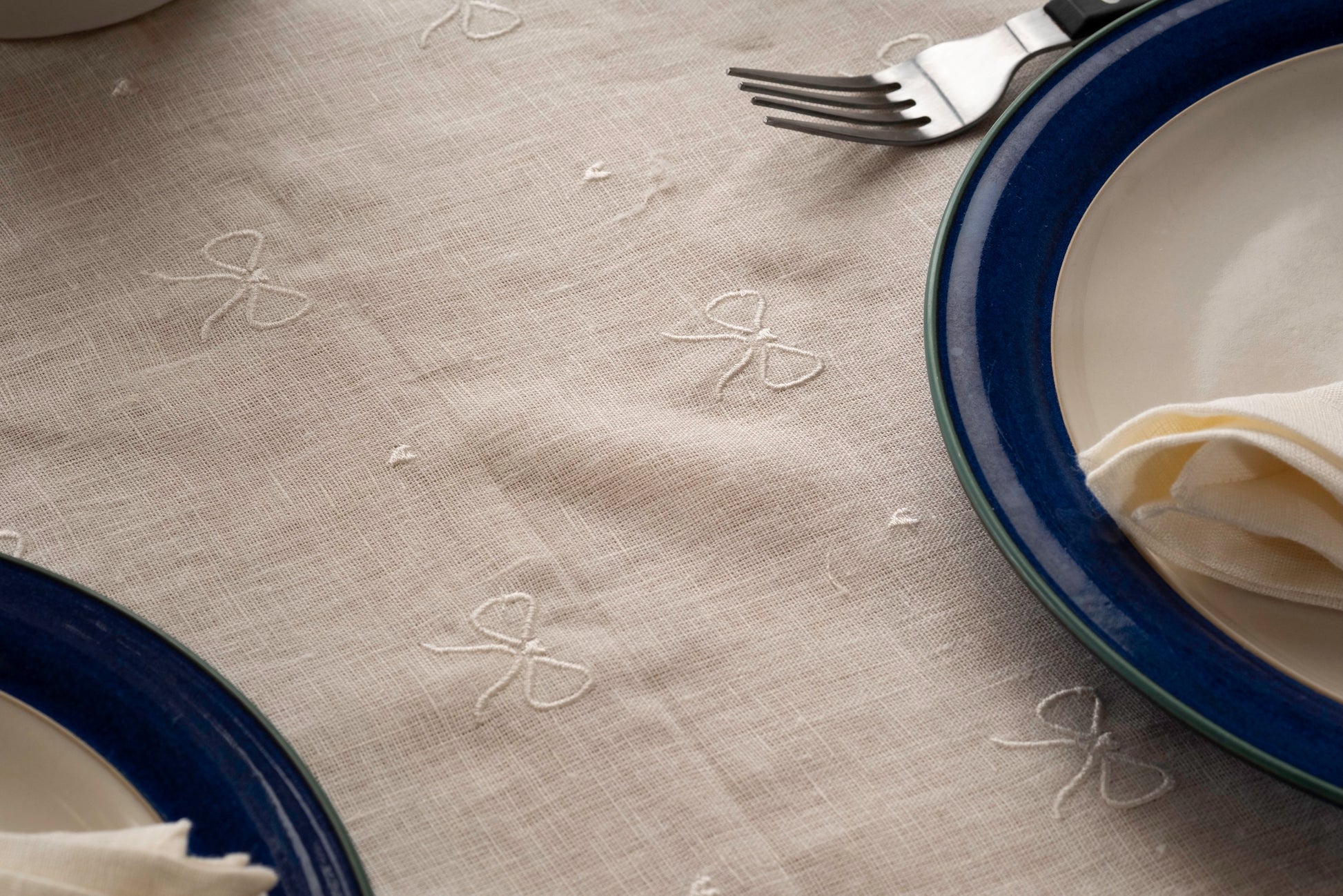 Off white tablecloth with embroidered ribbon embroidery and blue plates on a table.