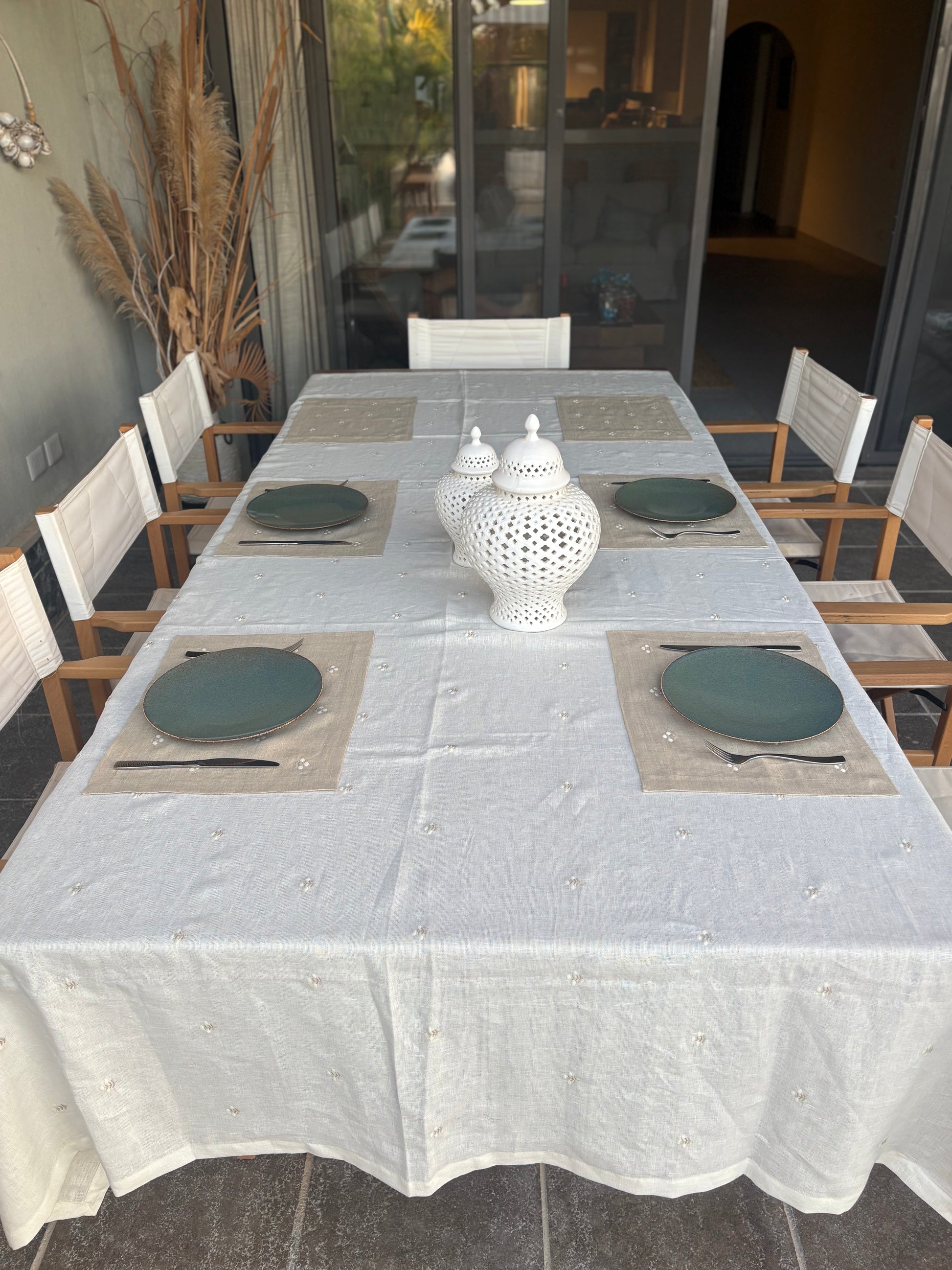 Dining table set with Egyptian linen placemats and decorative vases in a room with large windows.