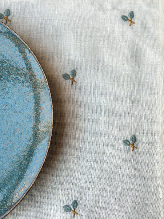 Blue ceramic plate on a textured beige tablecloth with embroidered designs.