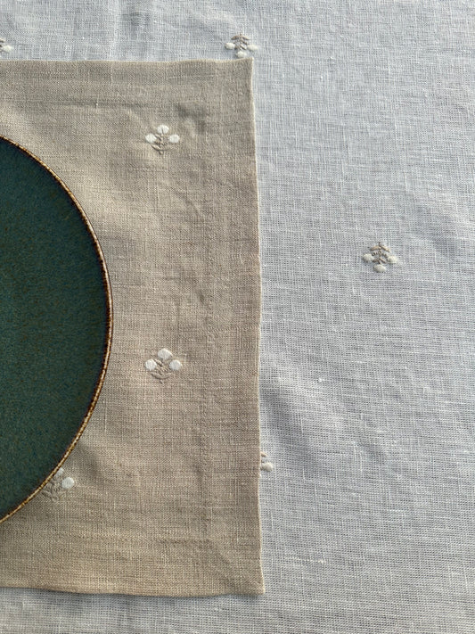 Close-up of a green plate with a brown rim on a beige linen placemat with minimal floral embroidery.