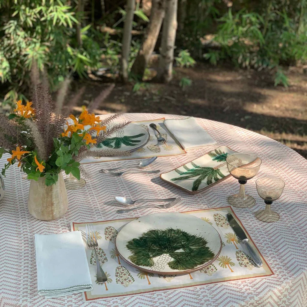 Outdoor table setting with floral arrangement, plates, and cutlery on a textured tablecloth.